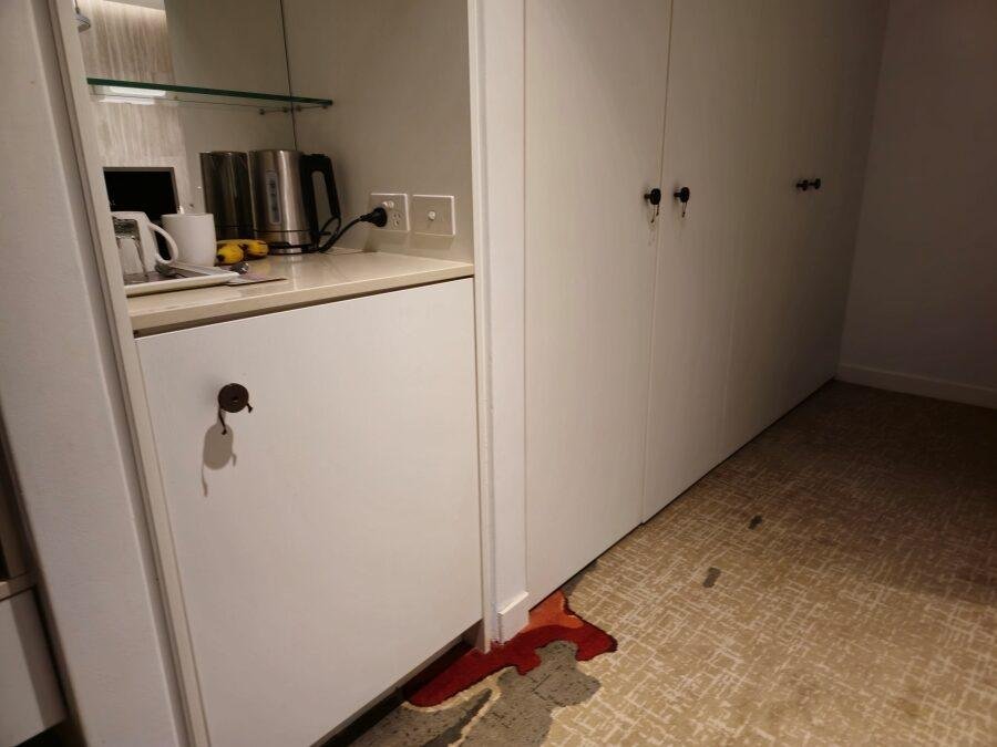 A white cabinet in a room with a kettle and cups on the counter.